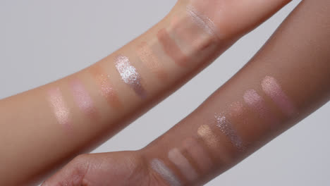 Close-Up-Of-Two-Women's-Arms-With-Colorful-Swatches-Of-Different-Glittery-Make-Up-Products